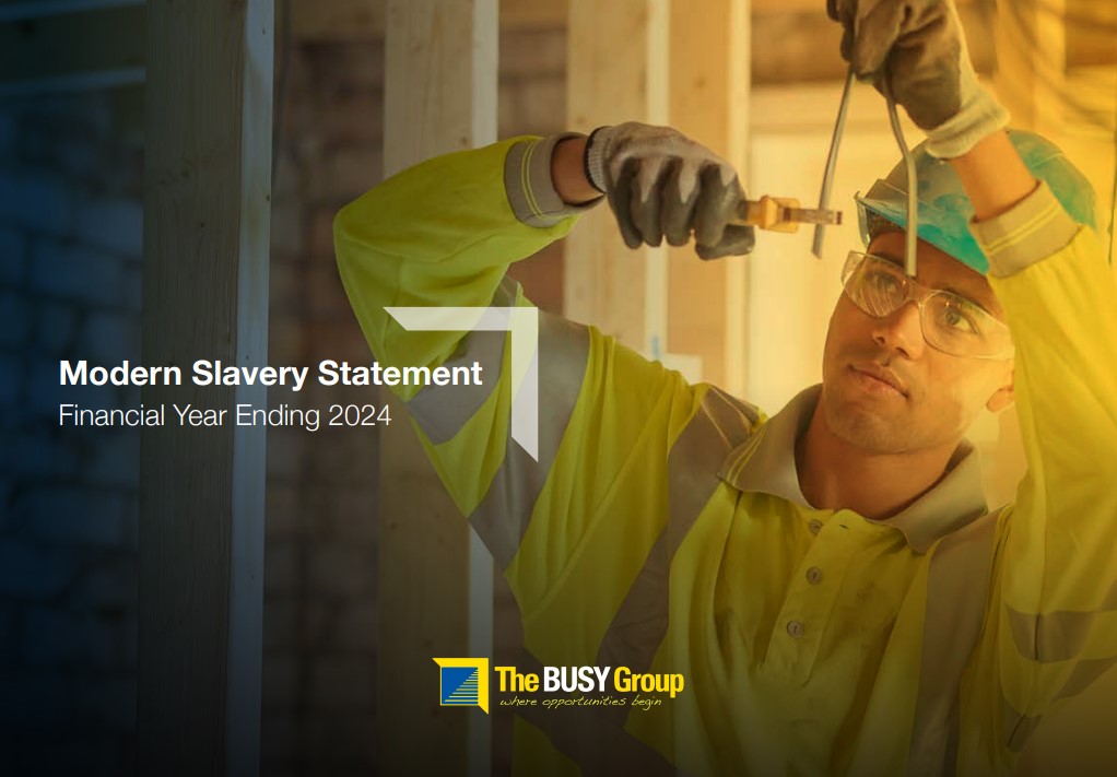 A construction worker wearing a yellow safety jacket and helmet uses a tool on a wooden frame. Text reads: Modern Slavery Statement, Financial Year Ending 2024, with support by Smart Apprenticeship Solutions. The BUSY Group logo appears at the bottom.